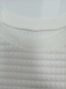Close-up of ribbed crew neck and waffle texture fabric on a white long sleeve sweatshirt