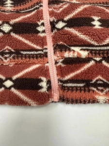 Detailed close-up of geometric pattern on rust red fleece jacket with pink resin zipper