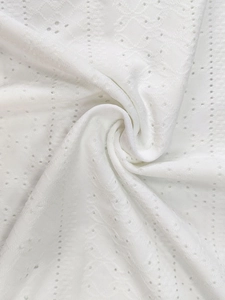 Detailed close-up of white bohemian dress fabric with hollow embroidery and lace patterns