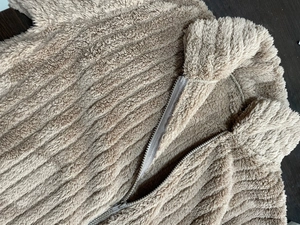 Dettaglio della giacca beige in pile a costine con cerniera in metallo su legno