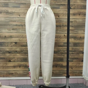 Detail of high waist joggers with drawstring and colorful side embroidery on cream fabric