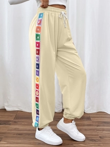 Detail of light beige sweatpants featuring colorful floral crochet side stripes and drawstring