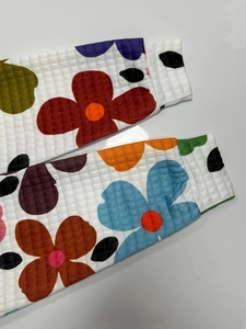 Dettaglio dei polsini in maglia a nido d'ape con motivo floreale retrò colorato sul tessuto