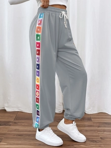Detail of grey sweatpants featuring colorful crochet floral side stripes and ribbed cuffs