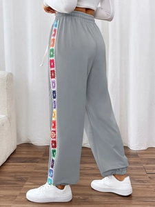 Detail of grey joggers featuring vibrant multi-colored crochet side stripes and drawstring