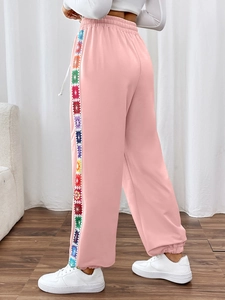 Detail of pink joggers featuring colorful crochet side stripes and elastic drawstring waist