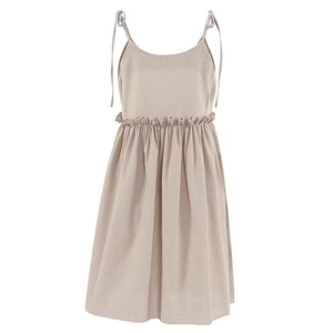 Detail of a beige cotton linen dress showing adjustable tie straps and ruffled waistline