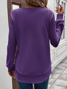 Outdoor street view of a women's purple waffle knit sweatshirt with a layered hem detail