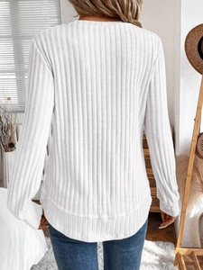 Detail view of white ribbed knit top showing curved hem and vertical texture