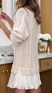 Detail view of beige cable knit sweater with side slit and white pleated skirt hem