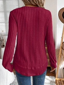 Detail of ribbed knit texture on long sleeve burgundy top with curved hem and crew neck