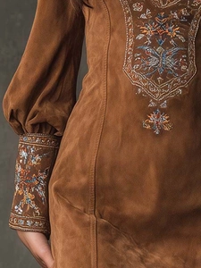 Detailed close-up of bohemian floral embroidery on brown suede lantern sleeves