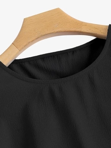 Détail du col rond d'un chemisier noir avec texture plissée sur un cintre en bois