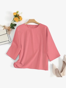 Détail d'un haut rose corail à col rond avec manches 3/4 et accessoires élégants