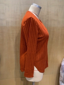 Detail of ribbed knit texture and side slit on an orange long sleeve V-neck top