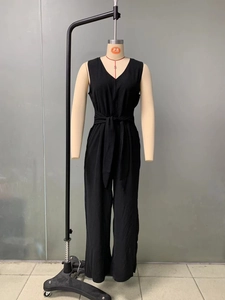 Detail of black V-neck sleeveless jumpsuit featuring a cinched waist and tie belt design