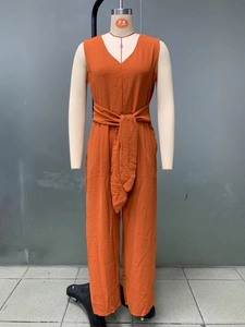 Detail of burnt orange V-neck jumpsuit showing textured fabric and waist tie belt