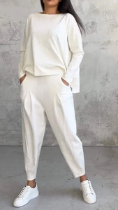 Dettaglio di top bianco a maniche lunghe e pantaloni a vita alta pieghettati su modella