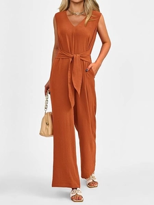 Detail of elegant rust red sleeveless jumpsuit with deep V-neck and belted wide leg design