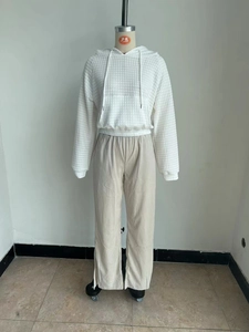 Detail of white waffle texture hoodie and beige corduroy trousers with side slit