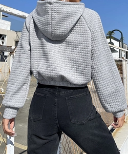 Close-up of grey waffle knit hoodie featuring cropped elastic waist and textured fabric detail