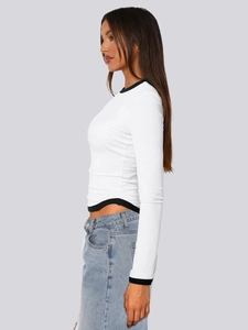Λεπτομέρεια λευκού crop top με μακριά μανίκια, μαύρα τελειώματα και καμπυλωτό στρίφωμα