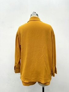 Détail d'une chemise jaune à manches longues avec tissu texturé et poignets boutonnés