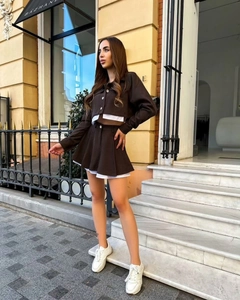 Detail view of deep brown pleated mini skirt and matching long-sleeve top with white trim