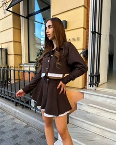Detail view of brown two-piece set featuring a cropped jacket and pleated mini skirt