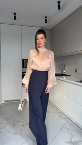 Close-up of champagne satin blouse with pleated collar and high-waist blue trousers