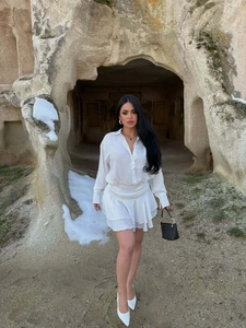Dettaglio di un completo bianco due pezzi con camicia a maniche lunghe e minigonna a balze