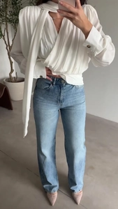 Detail of elegant white pleated blouse with bow ribbon and high-waist straight jeans