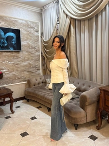 Detail of white off-shoulder top with ruffled cuffs and blue flared high-waist jeans