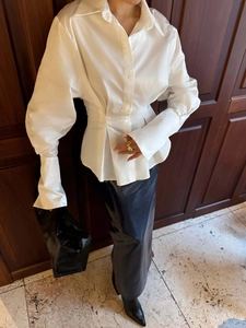 Detail of white pleated waist shirt with wide cuffs and elegant button accents