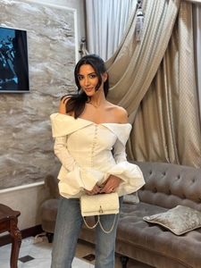 Detail of white off-shoulder long sleeve top with ruffle cuffs and decorative buttons