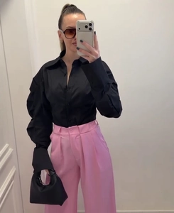 Detail of black lapel blouse with ruffled sleeves paired with pink pleated trousers