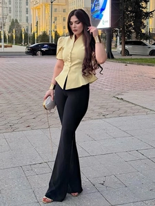 Detail of a light yellow short sleeve peplum shirt with buttons and black flared pants