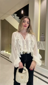 Close-up of white ruffle blouse with V-neck, lantern sleeves, and black high-waist pants