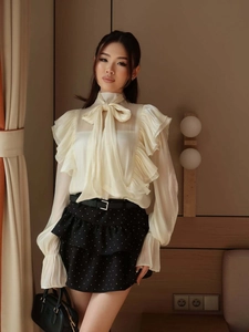 Detail of chiffon blouse featuring neck bow tie and layered ruffle sleeves with flared cuffs