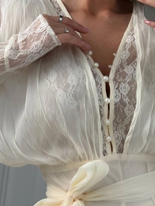 Dettaglio di pizzo elegante, bottoni perlati e scollo a V su un abito in chiffon crema