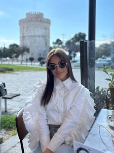 Detail of white cotton shirt featuring dramatic tiered ruffles on long sleeves in urban setting