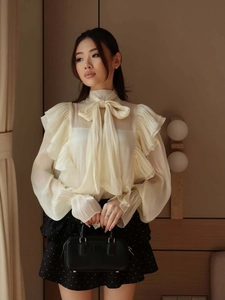 Detail of cream ruffle blouse with silk satin bow and elegant mock neck design