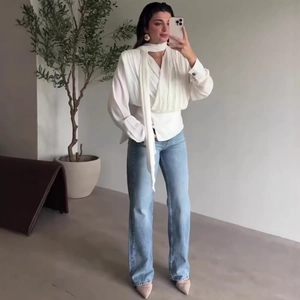 Elegant white long sleeve blouse with pleated drape and tie-neck paired with jeans