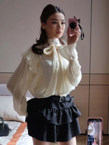 Detail of elegant cream chiffon blouse with ruffles and a chic black polka dot skirt