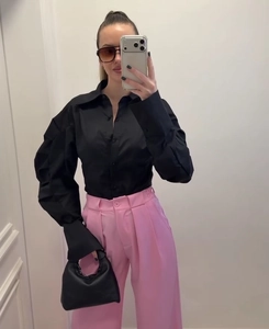 Detail of a black lapel shirt with pleated sleeves paired with pink high waist trousers