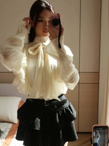 Detail of ruffled cuffs and bow-tie neck on a beige chiffon long-sleeve blouse