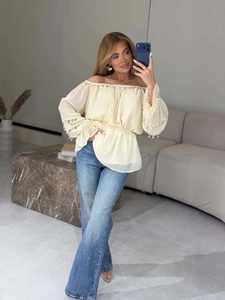 Detail of off-white off-shoulder blouse with sequins and fringe on collar and cuffs