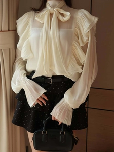 Detail of elegant beige chiffon shirt featuring ruffled sleeves and a large bow tie neck