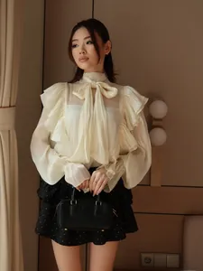 Close-up of cream bow-tie collar shirt with elegant ruffle details and long sleeves
