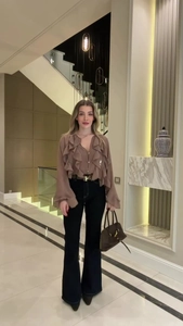 Detail view of khaki V-neck ruffle blouse paired with black flare jeans and gold H belt